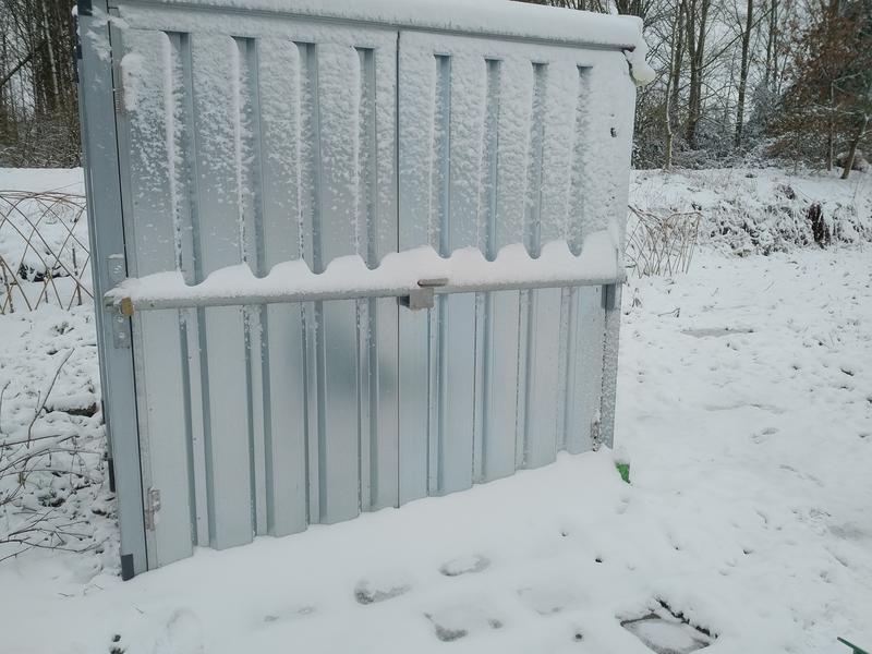 Metalen zelfbouwcontainer volledig ondergesneeuw. De metalen balk die over de deur zit is vastgevroren en er ligt 15cm sneeuw op.